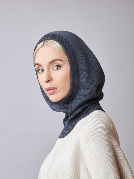European Muslim woman with a blonde hair in a bonnet hood dressed on her head. Beautiful girl in sweater with soft skin, natural cosmetics - Φωτογραφία, εικόνα