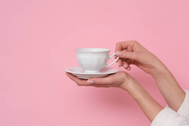 Coffe mood. Woman in white bath robe is holding a cup of coffee. Studio shoot on pink background. - Foto, afbeelding