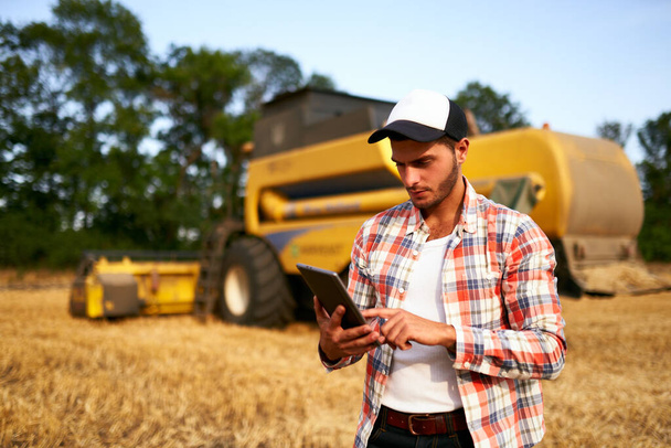 Precision farming. Farmer holding tablet for combine harvester guidance and control with modern automation system. Agronomist using online data management software generating yield maps at wheat field - Fotó, kép