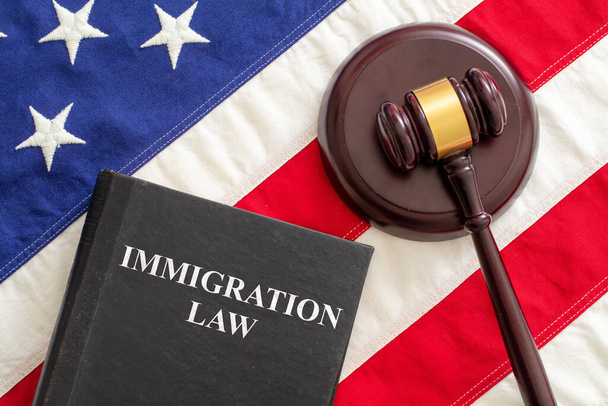 Tekst ustawy imigracyjnej o czarnej księdze i młotku sędziego na tle flagi USA, widok z góry. Migracja, wiza emigracyjna w USA - Zdjęcie, obraz
