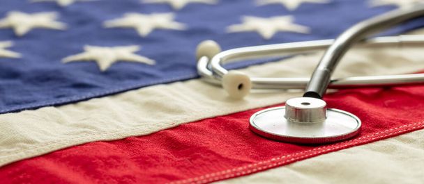 USA health care. Medical stethoscope on a US of America flag, closeup view, banner. American health insurance  concept - Фото, зображення