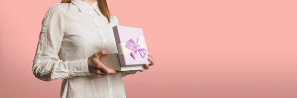молода дівчина відкриває подарункову коробку на світло-рожевому тлі. Обличчя дівчини відрізане
. - Фото, зображення