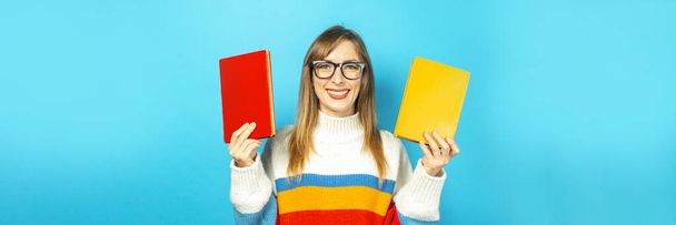 Молода жінка посміхається і тримає книжки в руках на синьому фоні. Концепція освіти, коледжу, сесії, іспиту, вибору кар'єри. Банер. - Фото, зображення