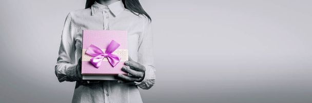 Молода дівчина відкриває перед собою подарункову коробку. Обличчя дівчини не видно. Чорно-біле зображення з кольоровим вибором подарункової упаковки
. - Фото, зображення