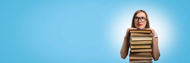 Ein junges Mädchen in weißem Kleid und Sonnenbrille legt die Hände auf einen Stapel Bücher vor blauem Hintergrund. Konzept der Bildung und des Lesens von Büchern. Banner. Kopierraum. - Foto, Bild