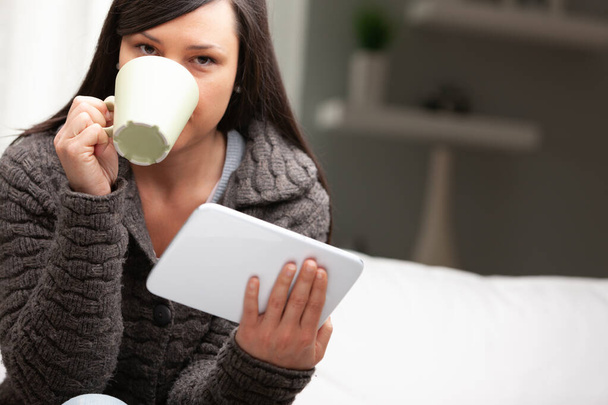 mujer en su sala de estar desayunando con la taza de la tableta y brioche, leyendo noticias y comenzando su trabajo desde casa
 - Foto, Imagen