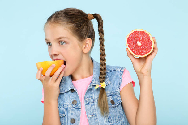 Young girl eating grapefruit on blue background - Фото, зображення