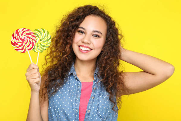 Young american girl holding colorful lollipops on yellow background - Fotó, kép