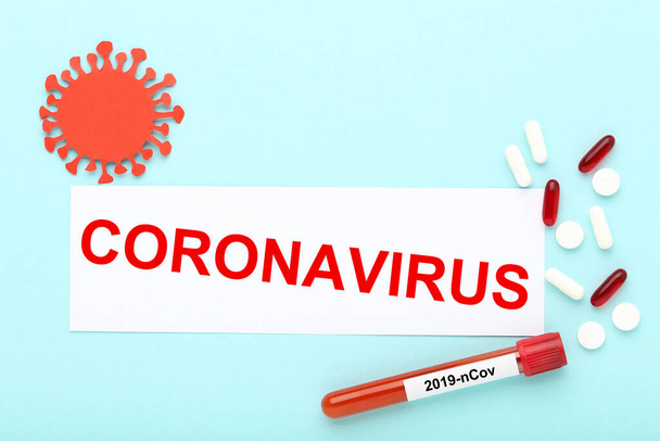 Text Coronavirus with pills and test tube with blood on blue background - Valokuva, kuva