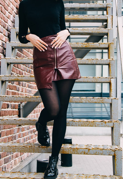 jovem mulher em uma saia de leopardo com calças de nylon pretas e uma camisola em uma jaqueta de couro contra uma parede de tijolo
 - Foto, Imagem
