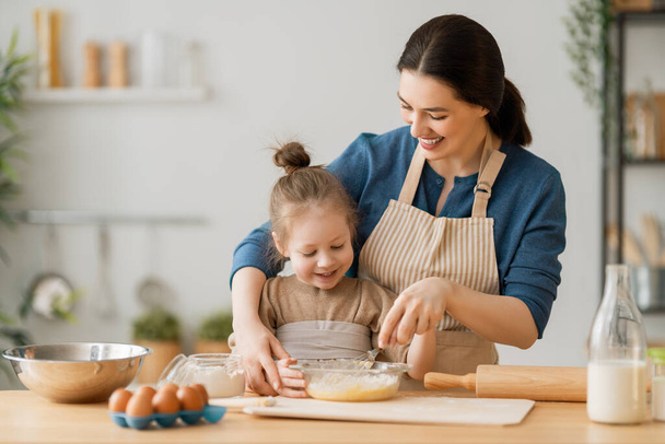 Happy loving family are preparing bakery together. Mother and child daughter girl are cooking cookies and having fun in the kitchen. Homemade food and little helper.    - Foto, Imagen