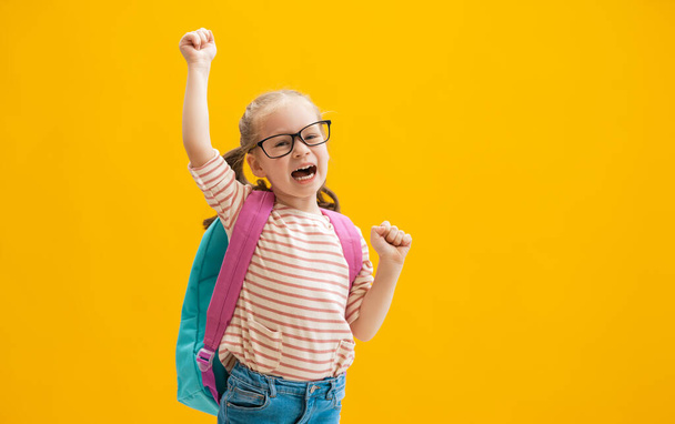 Back to school and happy time! Cute industrious child on color paper wall background. Kid with backpack. Girl ready to study. - 写真・画像