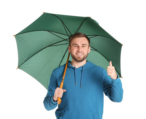 Όμορφος νεαρός με ομπρέλα που δείχνει τον αντίχειρα πάνω στο λευκό φόντο - Φωτογραφία, εικόνα