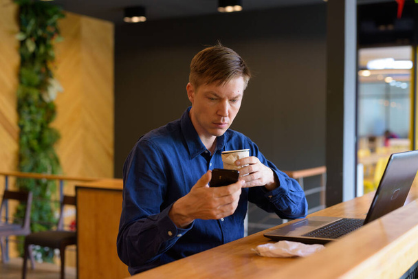 Young handsome Scandinavian businessman social distancing inside the coffee shop to prevent the spread of covid-19 - Фото, изображение