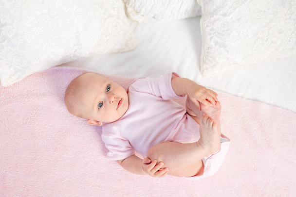 uma menina pequena 6 meses de idade está deitada em uma cama branca e rosa em casa, olhando para o lado, vista superior, lugar para texto
 - Foto, Imagem
