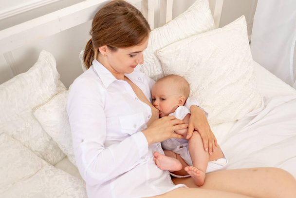 mom breastfeed baby 6 months old lying on a white bed, baby feeding, place for text - Fotó, kép