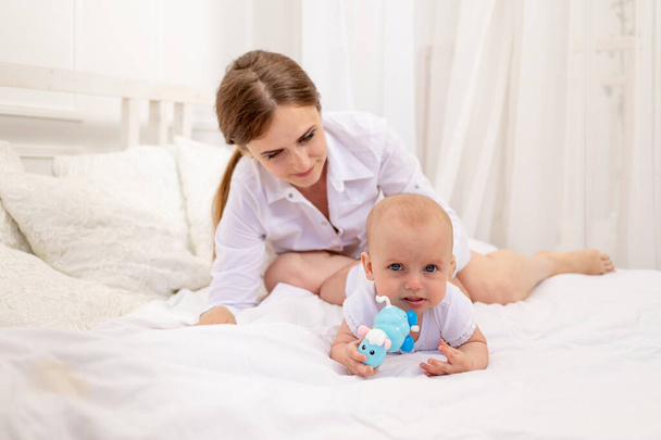 mam spelen met baby 6 maanden liggend op een wit bed, vrije tijd moeder met baby, plaats voor tekst - Foto, afbeelding