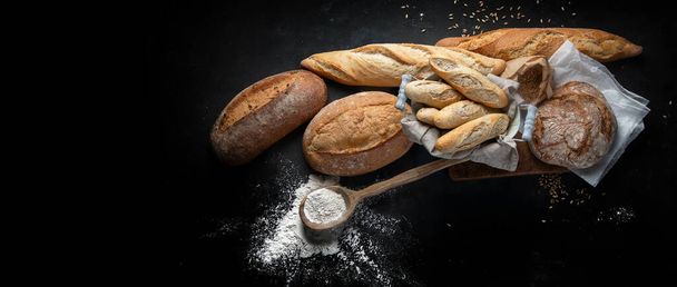 Fresh bread and buns on black background with copy space. View from above. Panorama, banner with copy space - Photo, image