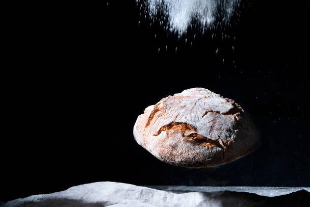freshly baked bread with flour splash  flying on black background - Фото, изображение
