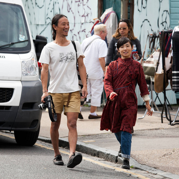 London, UK - 17 July 2019, Columbia Road Flower Market. A man in a white T-shirt and yellow shorts and a woman in a burgundy dress make their way through the crowd. - Foto, immagini