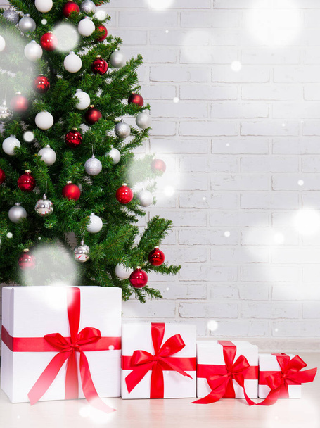 fondo de Navidad - cajas de regalo bajo el árbol de Navidad decorado sobre la pared de ladrillo y copos de nieve voladores
 - Foto, imagen