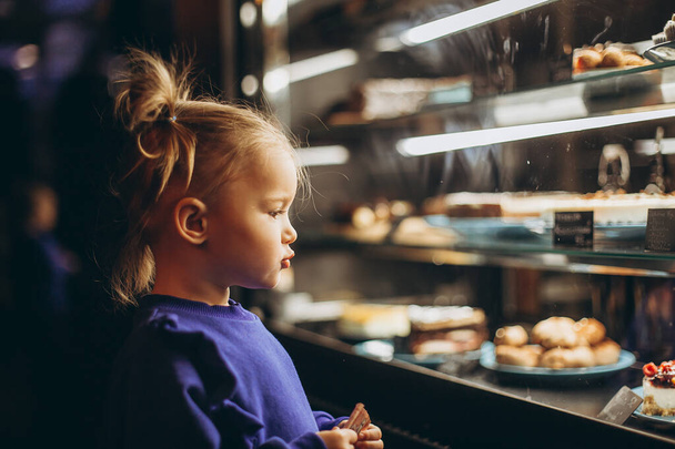 lovely girl admiringly examines a lighted showcase with various delicious cakes and desserts - Фото, зображення