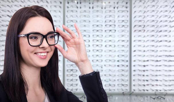 концепция зрения и зрения - счастливая молодая женщина примеряет очки в магазине оптики
 - Фото, изображение