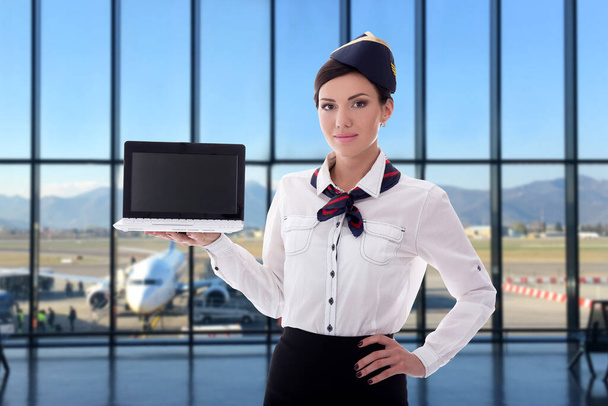 estate, vacanza e concetto di viaggio - bella hostess che tiene il computer portatile con schermo vuoto in aeroporto - Foto, immagini