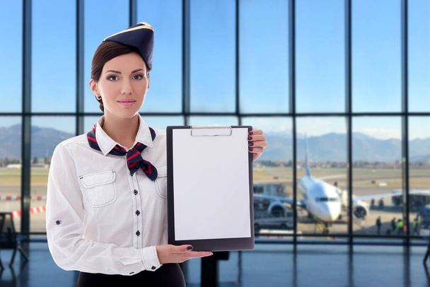 summer, vacation and travel concept - beautiful stewardess holding blank clipboard in airport - Photo, Image