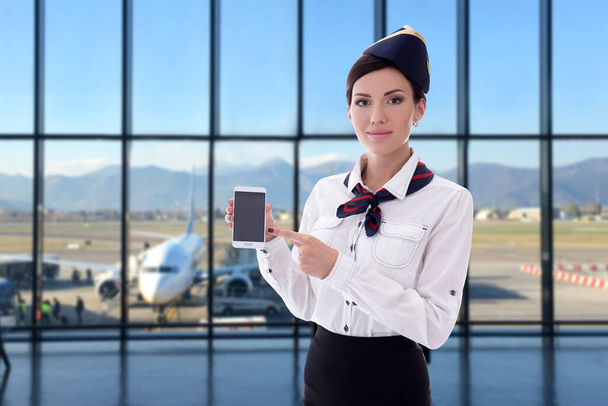 καλοκαίρι, διακοπές και ταξιδιωτικό concept - όμορφη αεροσυνοδός κρατώντας έξυπνο τηλέφωνο με κενή οθόνη στο αεροδρόμιο - Φωτογραφία, εικόνα