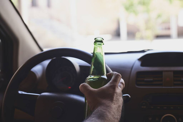 A bottle of beer in a man's hands driving the car during daytime - Fotografie, Obrázek
