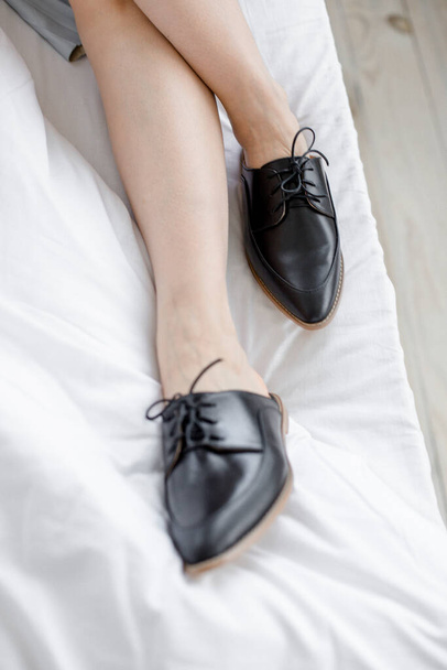 girl takes off her office shoes in a room in bed on white bedding, is tired after work and is resting, morning of the working day in shoes in bed - Фото, изображение