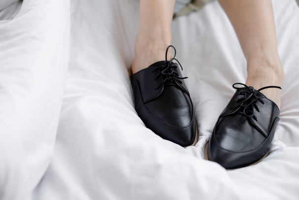 girl takes off her office shoes in a room in bed on white bedding, is tired after work and is resting, morning of the working day in shoes in bed - Fotoğraf, Görsel