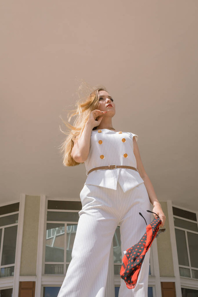 A beautiful white girl posing in the background of a city building. The girl is dressed in a white suit. She has gorgeous hair and makeup - Foto, afbeelding