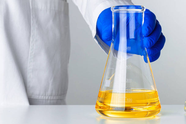 Scientist or doctor in blue gloves pouring some yellow liquid into a flask - Фото, изображение