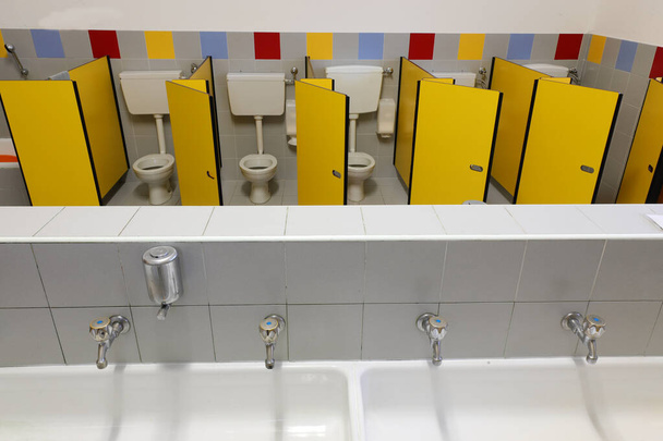 длинная раковина с четырьмя кранами в детском саду с туалетами с желтыми дверями без детей
 - Фото, изображение