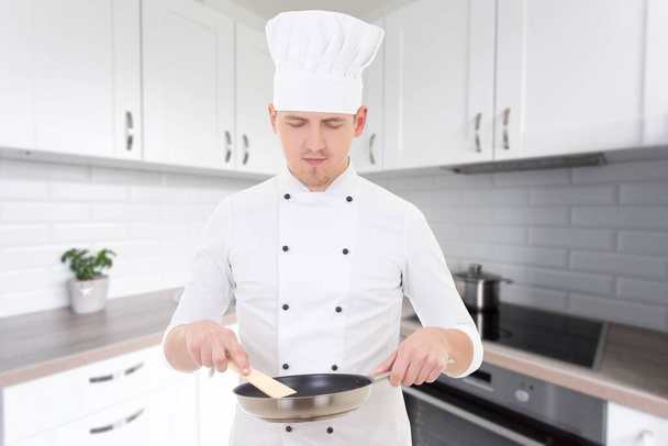 portrait of man chef in uniform holding frying pan in modern kitchen - 写真・画像