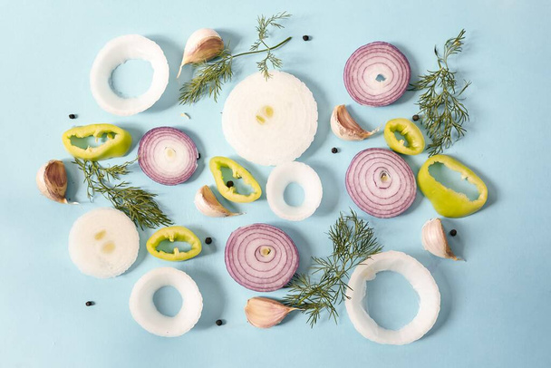 A top view of raw onion rings with yellow pepper, peppercorns, garlic and dill on a blue surface - Foto, imagen