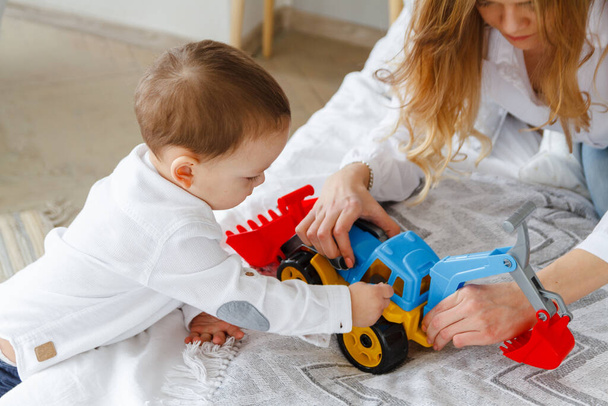 Young mother and cute son playing together with a toy tractor sitting on the bed - 写真・画像