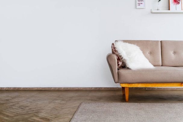 Element of a stylish beige sofa with a white fluffy pillow against a white wall background - Fotó, kép