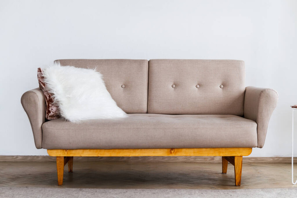 Stylish beige sofa with a white fluffy pillow against a white wall background - Foto, afbeelding