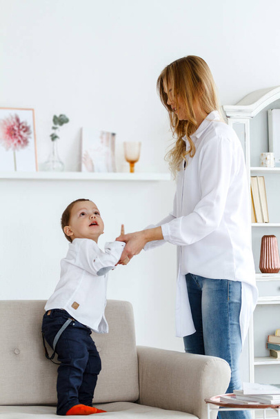A young mother with a cute little son is having fun in a bright cozy living room - Φωτογραφία, εικόνα