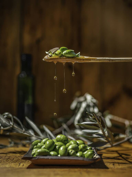 Focus verticale selettivo di olive verdi con foglie e olio di oliva sullo sfondo - Foto, immagini