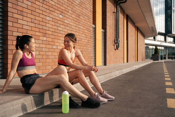 Portrait of two young beautiful sport woman resting after workout in the city - Photo, Image