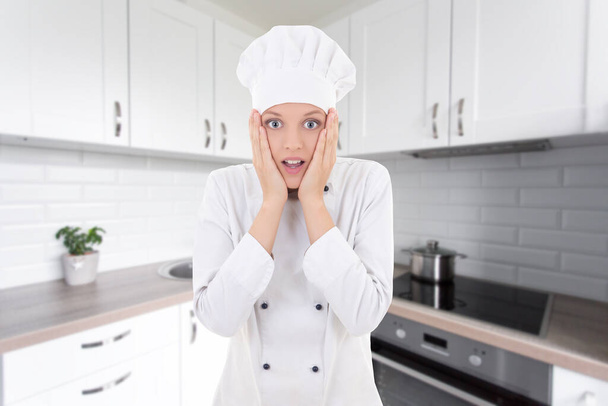 funny shocked woman in chef uniform in white modern kitchen - Photo, Image