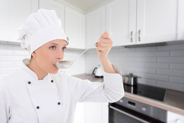 молода жінка в кулінарній уніформі дегустація чогось на сучасній кухні
 - Фото, зображення