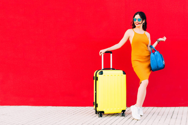 χαρούμενη γυναίκα με γυαλιά ηλίου, κίτρινη βαλίτσα και μπλε τσάντα. - Φωτογραφία, εικόνα