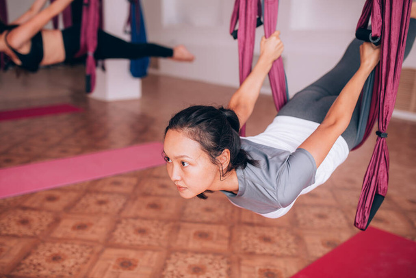 Schöne junge Mädchen machen Fly Yoga auf Hängematten, strecken den Rücken, entspannen auf Gewicht, kümmern sich um die Gesundheit. - Foto, Bild