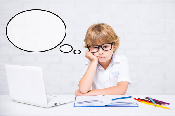 нудний маленький школяр в окулярах робить домашнє завдання вдома і думає про щось
 - Фото, зображення