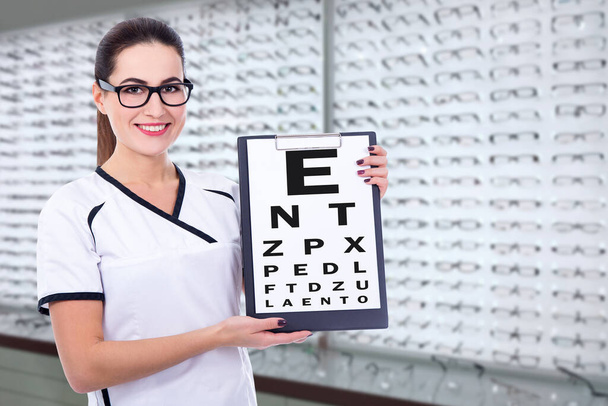 Optometrista o consultora joven sosteniendo portapapeles con gráfico de prueba de visión visual en la tienda de óptica
 - Foto, imagen